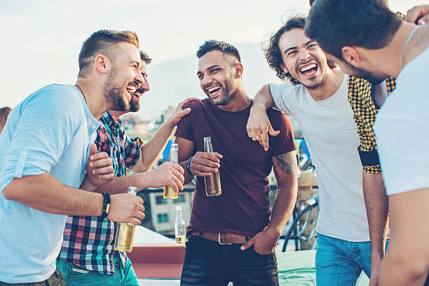 Boys drinking beer and having fun Multi-ethnic group of young men chatting and drinking beer on a rooftop party. stag night stock pictures, royalty-free photos & images