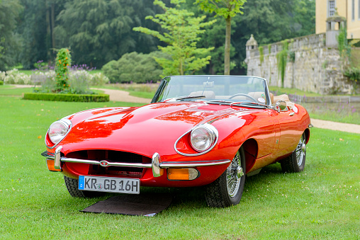 Jüchen, Germany - August 5, 2016: Jaguar E-Type Series 2 Roadster or Jaguar XK-E 1960s convertible sports car front view. The E-type is an iconic British sports car produced by Jaguar from 1961 until 1975 and was available as coupe or convertible. The car is on display during the 2016 Classic Days at castle Dyck. The car is displayed in a field.