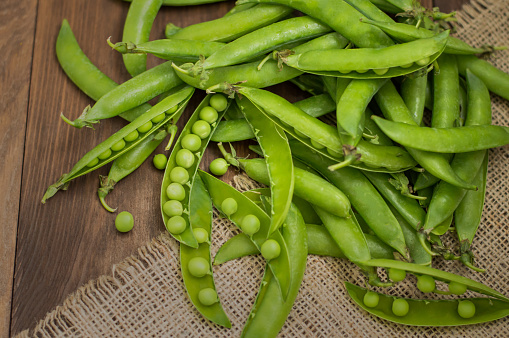 Pea pods on sacking. Wooden background. Top view