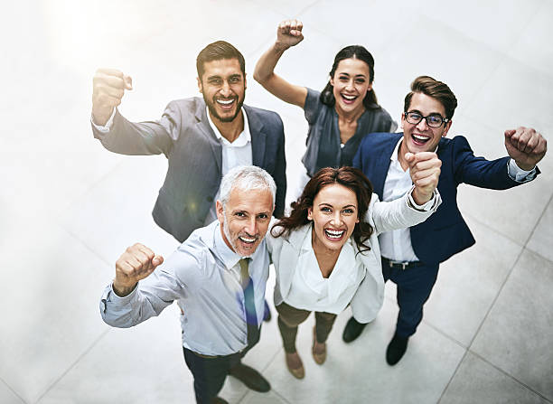 Teamwork saves the day High angle portrait of a diverse team of professionals cheering at work cheering group of people success looking at camera stock pictures, royalty-free photos & images