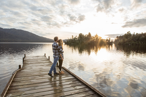 Cheerful young couple on a lake pier being affectionate. Lake Kaniere, New Zealand.