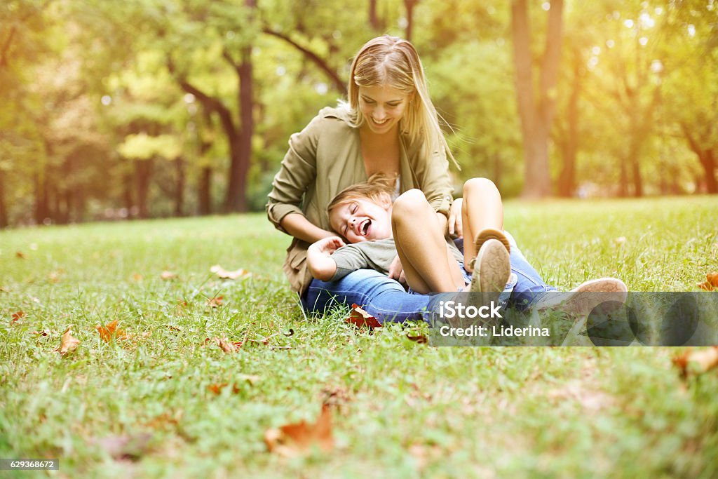 Mother with her daughter in the park. Little girl sitting on the mother lap. Cheerful mother with her daughter sitting in the grass. Space for copy. Grass Stock Photo