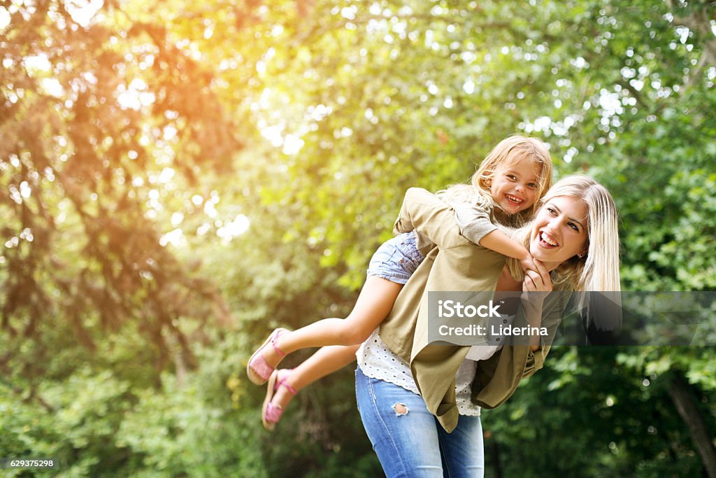 Little girl on a piggy back ride with her mother. Cute young daughter on a piggy back ride with her mother. Looking at camera. Family Stock Photo