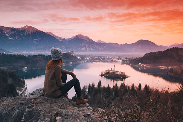 Travel Slovenia, Europe. Travel Slovenia, Europe. Woman looking on Bled Lake with Island, Castle and Alps Mountain on background. Top view. Bled Lake one of most amazing tourist attractions. Sunset winter nature landscape. gorenjska stock pictures, royalty-free photos & images