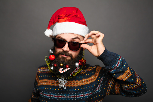 stylish modern Bad Santa concept. Young bearded man wearing sunglasses and santa claus hat. Close up portrait