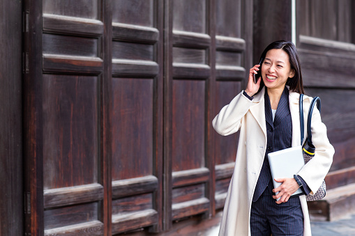 Business woman talking on the phone while walking and carrying a digital tablet