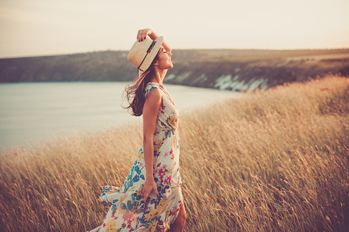 Side portrait of Modern girl in light summer dress with stylish hat enjoying sunset