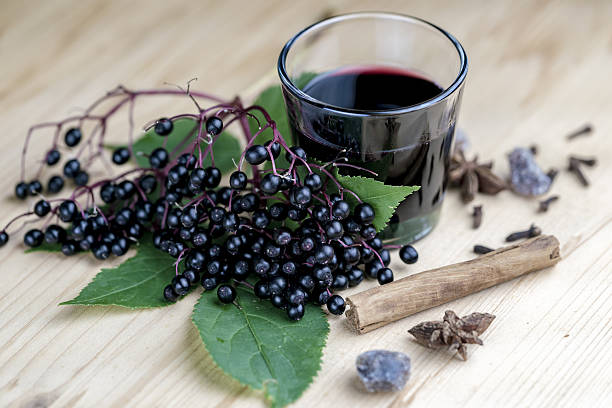 Glass of fresh elderberry syrup with ingredients Glass of fresh elderberry syrup with cinnamon stick, brown sugar, star anise and elderberries on a wooden kitchen counter elderberry photos stock pictures, royalty-free photos & images