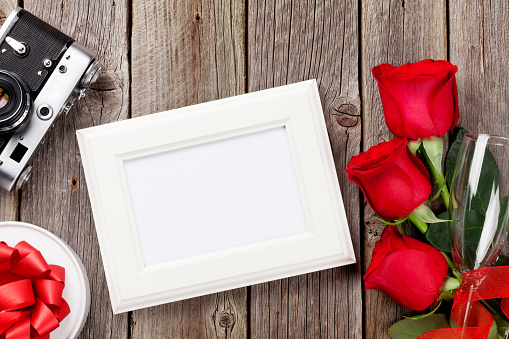 Valentines day roses, photo frame, retro camera and gift box over wooden background
