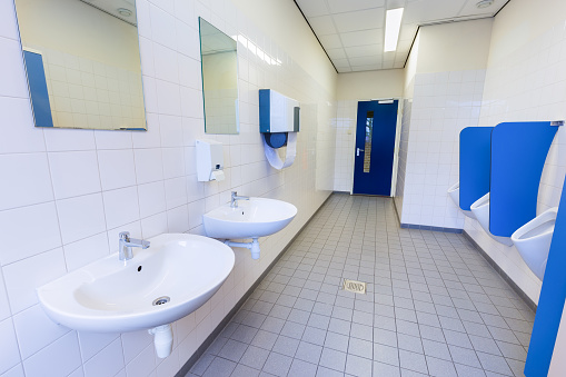 Toilet room for boys with urinals sinks and mirrors on high school. I took this photo in secondary school where I work. It's a typical men's room for school pupils. The wall tiles are white and some other parts are blue.
