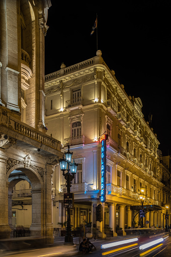 Havana, Cuba - October 12, 2016: Night time exterior of old Havana hotel Inglaterra. A Havana landmark, one of the oldest hotels in Cuba dating from 1875. Magnificent old Grand Theater  of Havana next door to old hotel of Inglaterra, on the main boulevard of Prado. This newly renovated colonial building was built in 1938 with grand hall that is now home of Cuban National Ballet. Early evening, people on the street. Local traffic passing by. 