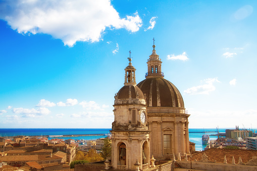Catania, Sicily: Beautiful old town panorama with vibrant orange tile roofs; the cupola of the 18th-century Duomo di Sant'Agata is in the foreground and a turquoise sea and harbor in the background.