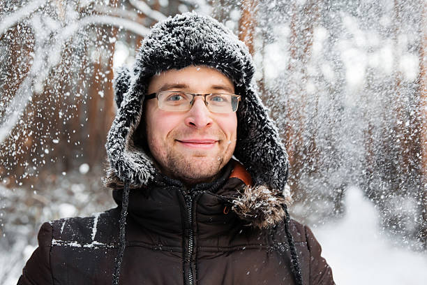 Man in fur winter hat with ear flaps smiling poextreme in the forest