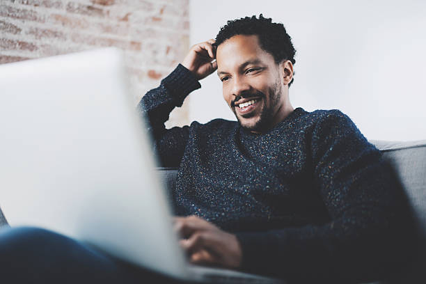 istock Cheerful bearded African man working on laptop while sitting sofa 629420022