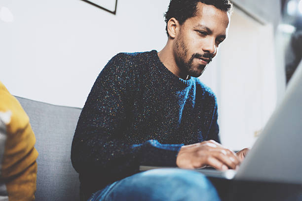 istock Young African man using laptop while sitting at his modern 629420370