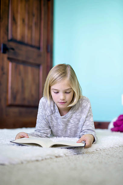 istock Cute young girl reading a challenging book on the floor 629421638