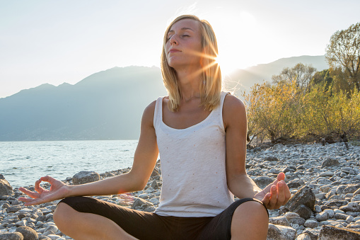 Portrait of a young woman by the lake exercising yoga at sunrise.