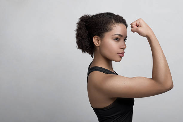 studioaufnahme einer jungen frau, die ihre muskeln beugt - flexing muscles stock-fotos und bilder