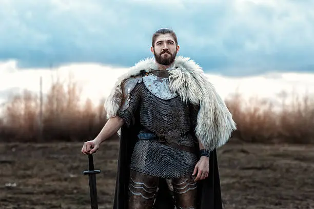 Formidable man warrior in armor and sword standing in a field and protects.