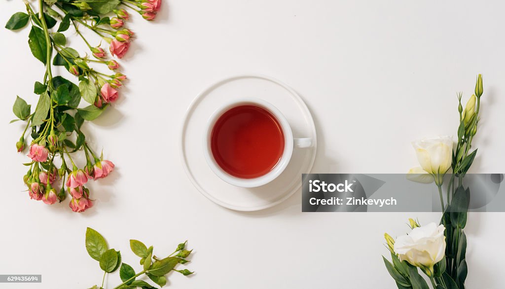 Top view of tea cup surrounded by flowers Herbal tea. Top view of a cup filled with herbal tea standing in the middle of the white desk while being surrounded by beautiful flowers Tea - Hot Drink Stock Photo
