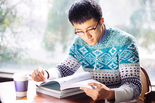 young asian man student with sweater reading book in library