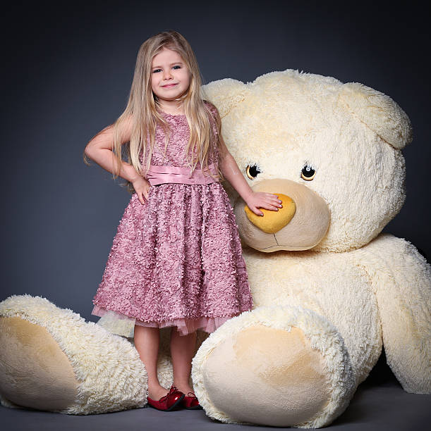 Little lady in dress touching teddy's nose Little lady in dress touching teddy's nose, stuffed animals, plush animals, big plush toys, kids and gifts, lilac dress, blonde girl, baby in studio, cerne abbas giant stock pictures, royalty-free photos & images
