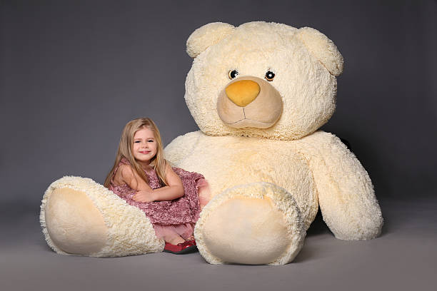Baby sitting on the large teddy bear Baby sitting on the large teddy bear, stuffed animals, plush animals, big plush toys, kids and gifts, lilac dress, blonde girl, baby in studio, cerne abbas giant stock pictures, royalty-free photos & images