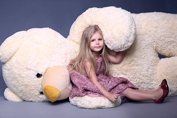 Little lady in lilac dress laying on the large teddy Little lady in lilac dress laying on the large teddy bear. cerne abbas giant stock pictures, royalty-free photos & images