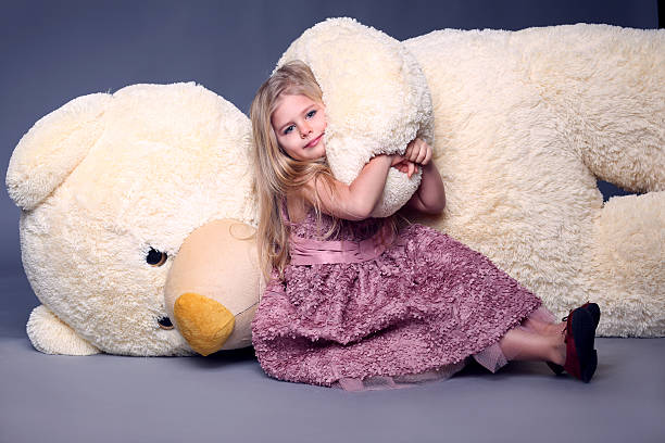 Baby in dress hugging big teddy's hand Baby in dress hugging big teddy's hand, stuffed animals, plush animals, big plush toys, kids and gifts, lilac dress, blonde girl, baby in studio, cerne abbas giant stock pictures, royalty-free photos & images