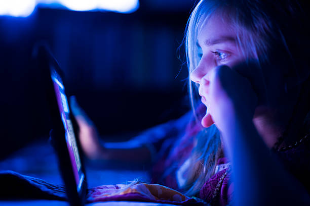 Teenager girl reading from tablet at night in the bed Beautiful long haired teenager girl reading from tablet, in the dark room at night in the bed, with her face illuminated by the screen 13 14 years child teenage girls lying down stock pictures, royalty-free photos & images