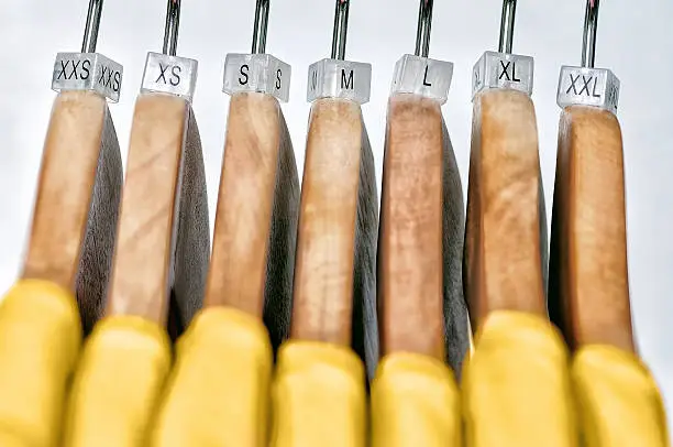 Yellow women's t-shirts hang on wooden hangers with indexes of the XXS, XS, S, M, L, XL, XXL sizes on a gray background.