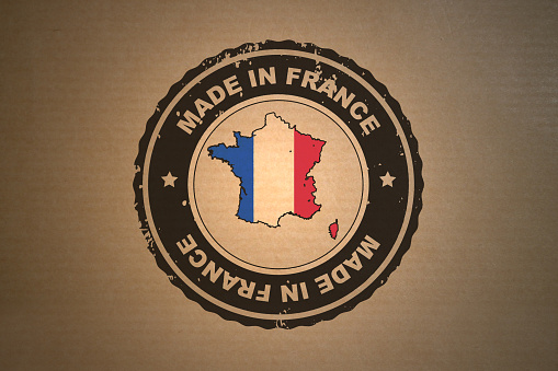 Close up on a “Made in France” stamp on a brown paper. The stamp has in its center a French flag shaped in a map of France.
