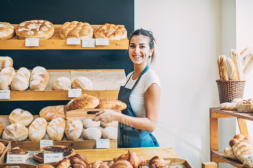 Young bakery owner holding a tray with bread in her shop.