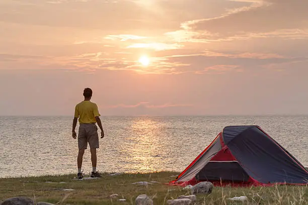 Sunrise in camping day. Alone tourist stands near tent and enjoy beautiful view.