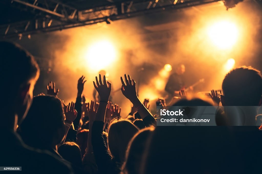 silhouettes of concert crowd in front of bright stage lights Silhouettes of people in a bright in the pop rock concert in front of the stage. Hands with gesture Horns. That rocks. Party in a club Rock Music Stock Photo