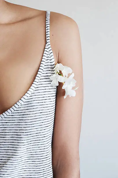 Cropped studio shot of a woman with a flower under her arm against a gray background