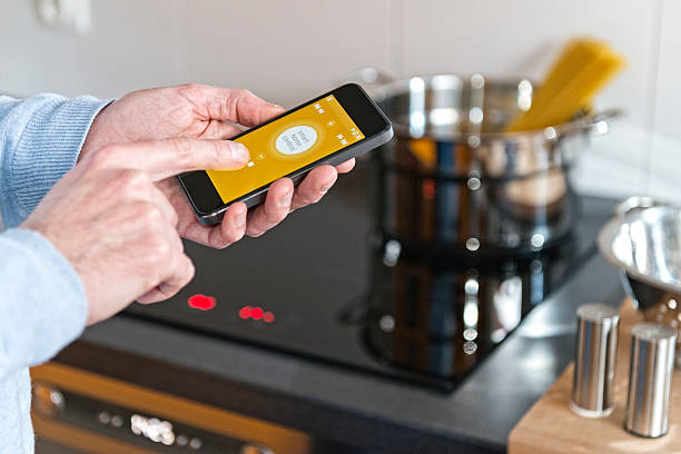 Man hand holding mobile phone smart control home cooker, kitchen stock photo