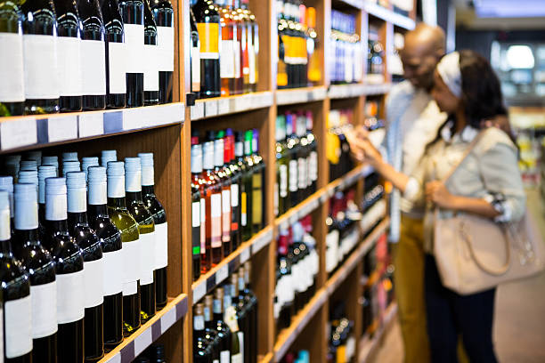 Couple looking at wine bottle in grocery section Couple looking at wine bottle in grocery section at supermarket liquor store counter photos stock pictures, royalty-free photos & images