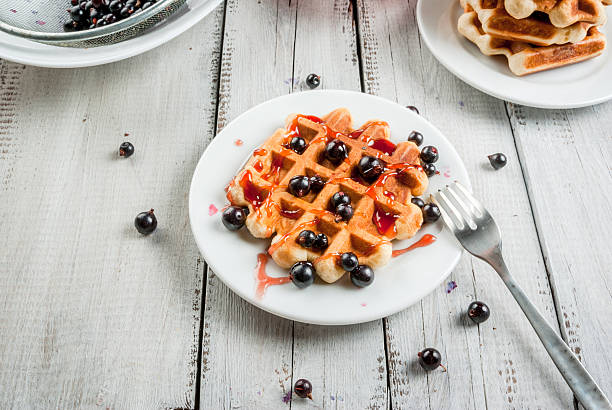 Homemade breakfast. Fresh Belgian waffles with summer berries and currant jam. On a white rustic wooden table.