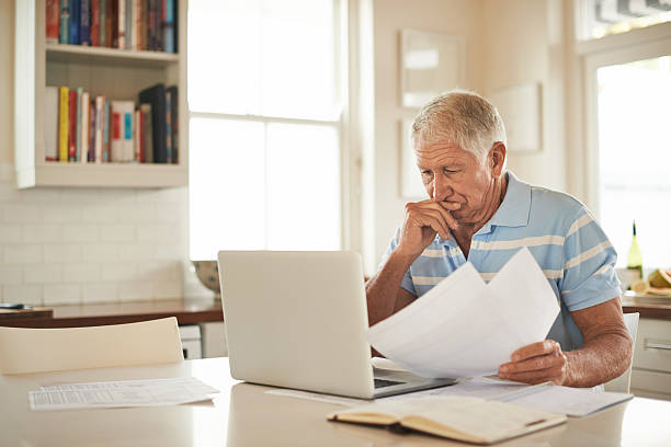 Everything's adding up... Shot of a senior man looking stressed while doing the household finances on a laptop in his kitchen man check stock pictures, royalty-free photos & images