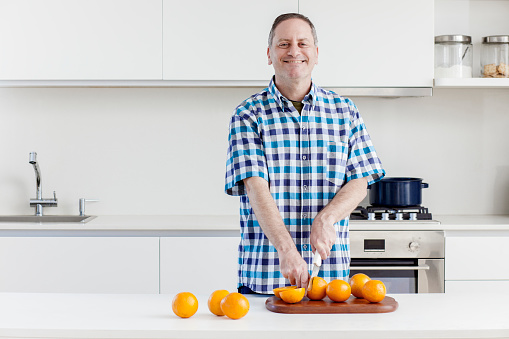 Middle aged man halving oranges on kitchen counter in modern kitchen