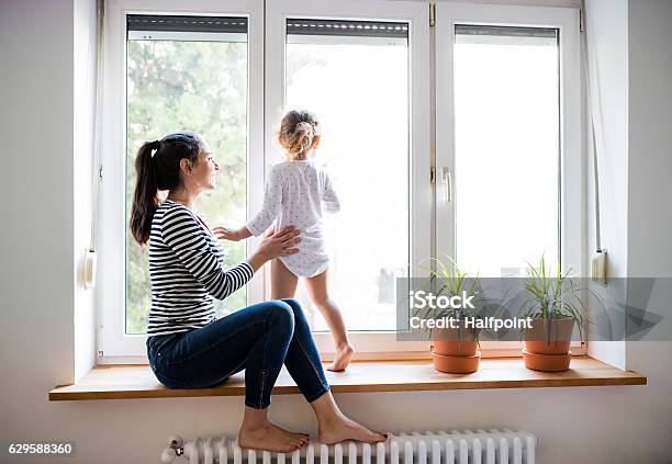 Mother With Her Little Daughter Looking Out Of Window Stock Photo - Download Image Now