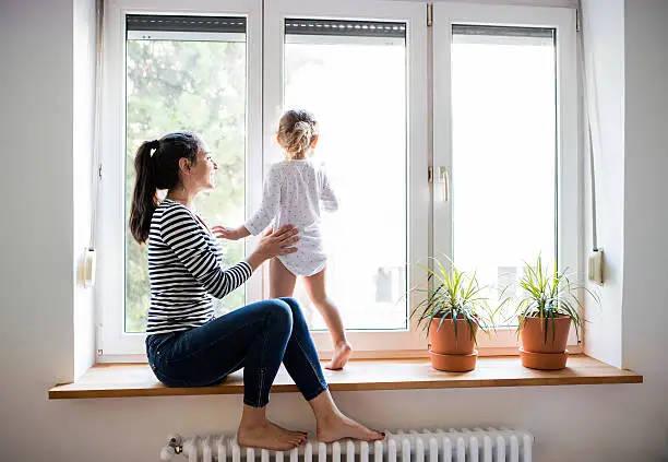 Photo of Mother with her little daughter looking out of window