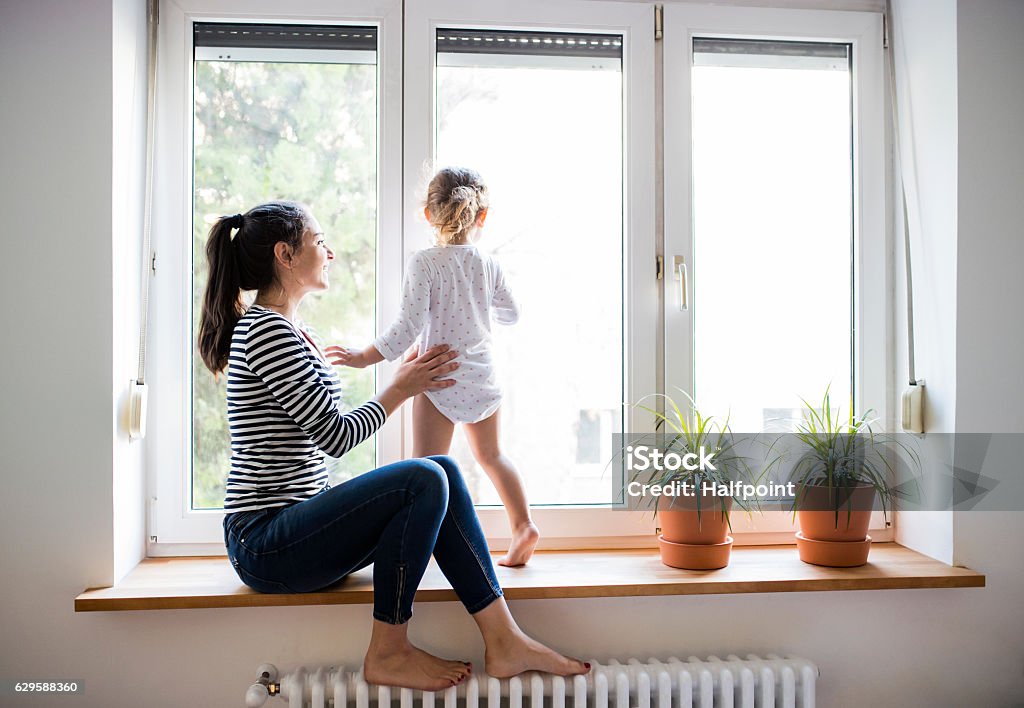 Mother with her little daughter looking out of window - Royaltyfri Fönster Bildbanksbilder