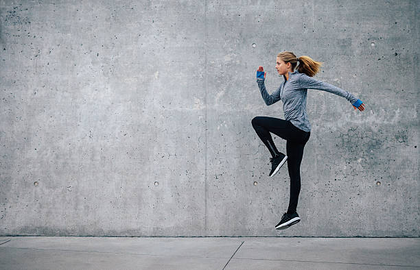 Fit young woman doing cardio interval training Side view shot of fit young woman doing cardio interval training against grey background. Fitness female exercising outdoors in morning. warming up stock pictures, royalty-free photos & images