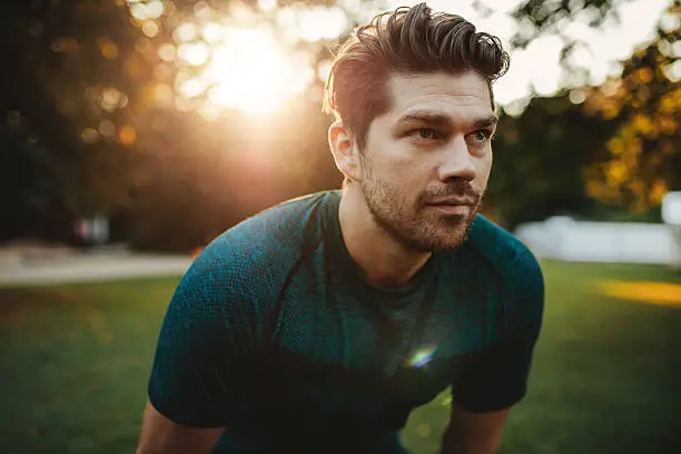 Close up portrait of healthy young man standing outdoors in park and looking away. Confident young man ready of workout.