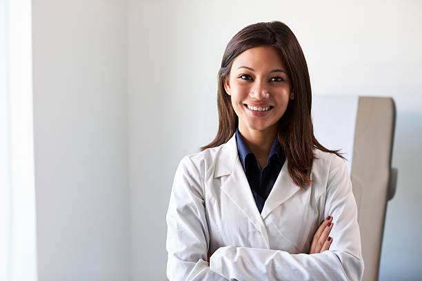 retrato de una doctora con bata blanca en la sala de exámenes - bata de laboratorio fotografías e imágenes de stock