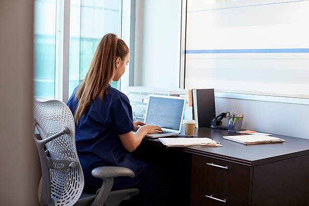 infermiera che indossa scrub che lavora alla scrivania in ufficio - laptop doctor using computer nurse foto e immagini stock