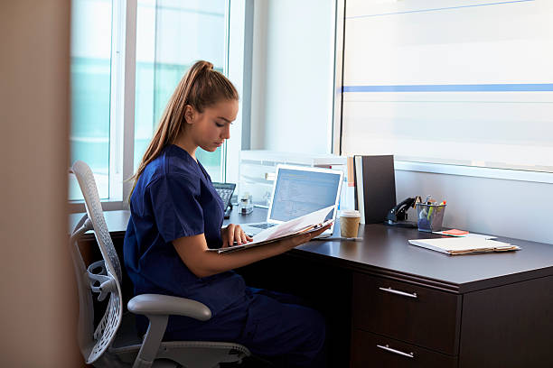 медсестра ношение скрабс, работающих на столе в офисе - laptop doctor using computer nurse стоковые фото и изображения