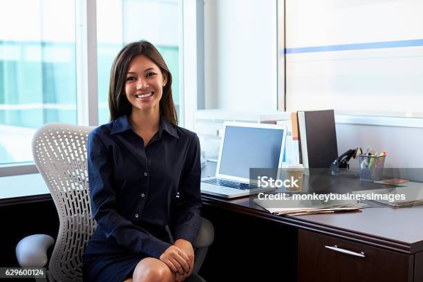 Portrait Of Female Doctor Sitting At Desk In Office Stock Photo - Download Image Now